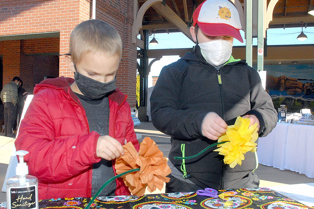 Alec Naddy, 6, left, and his brother, Porter Nady, 9, both of Bothell, create tissue paper marigolds on Saturday at the Port Angeles Farmers Market. The flowers will become part of a Día de los Muertos ofrenda, a display of mementos honoring deceased loved ones for the Day of the Dead, which will be set up at The Wharf mall next week. The craft event is co-sponsored by the Juan de Fuca Foundation for the Arts and North Olympic Library System. (Keith Thorpe/Peninsula Daily News)