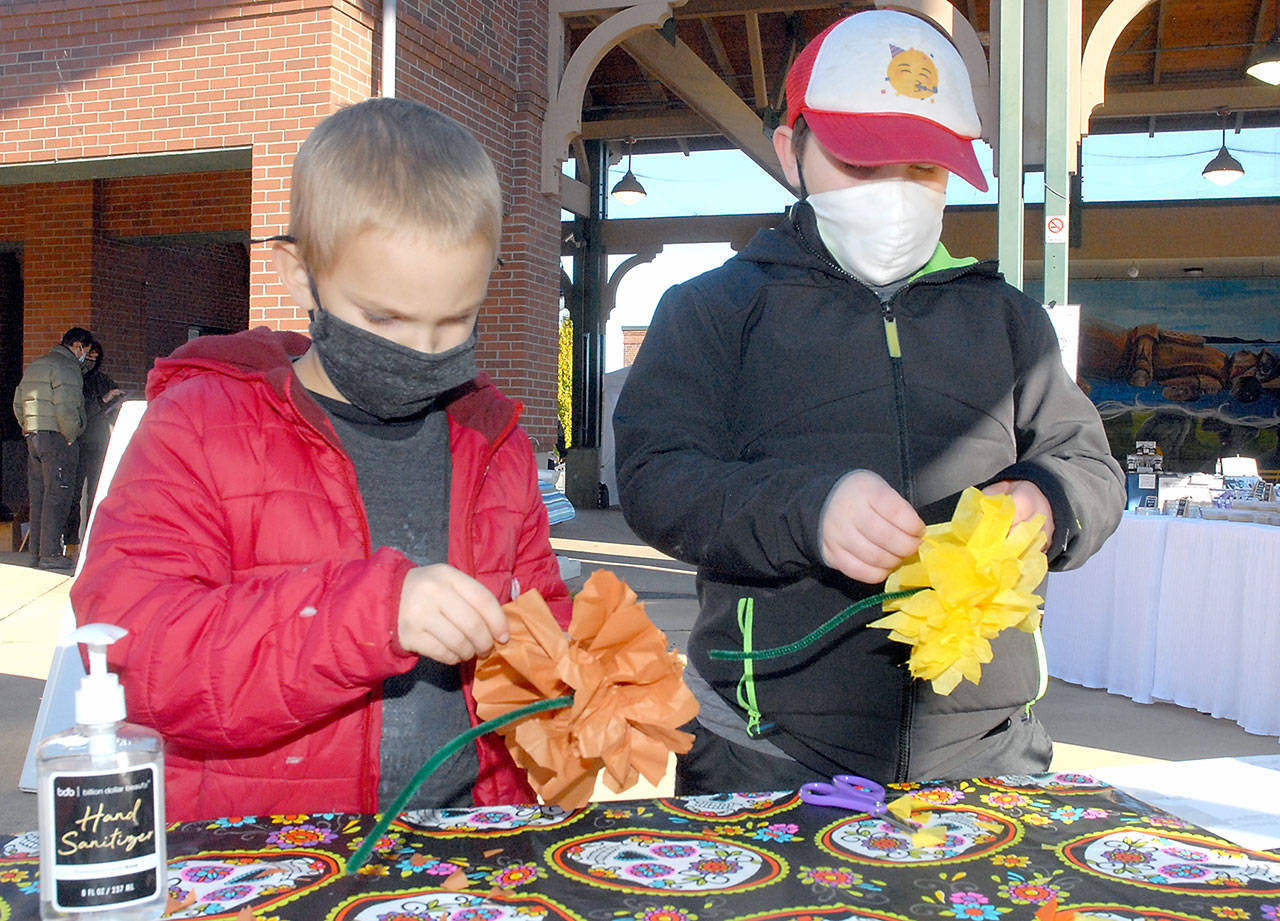 Alec Naddy, 6, left, and his brother, Porter Nady, 9, both of Bothell, create tissue paper marigolds Saturday, Oct. 24, 2020, at the Port Angeles Farmers Market. The flowers will become part of a Día de los Muertos ofrenda, a display of mementos honoring deceased loved ones for the Day of the Dead, which will be set up at The Wharf mall next week. The craft event is co-sponsored by the Juan de Fuca Foundation for the Arts and North Olympic Library System. (Keith Thorpe/Peninsula Daily News)