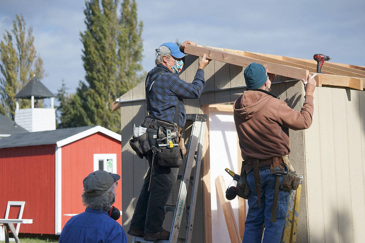 Blue Heron Construction co-owner Randy Welle, center, Greg Kossow, right, and Larry Morrell, bottom left, work on the roof overhang of an emergency shelter Thursday afternoon in Port Townsend. The neighbors formed a volunteer group to build one shelter over several days as part of the Community Build Project, which aims to provide temporary-use shelters for the homeless during the coming winter months. (Nicholas Johnson/Peninsula Daily News)