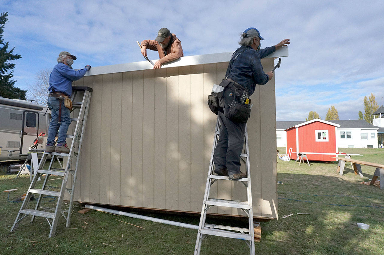 Larry Morrell, from left, Greg Kossow and Blue Heron Construction co-owner Randy Welle work to construct an emergency shelter Thursday afternoon in Port Townsend. The neighbors formed a volunteer group to build one shelter over several days as part of the Community Build Project, which aims to provide temporary-use shelters for the homeless during the coming winter months. (Nicholas Johnson/Peninsula Daily News)