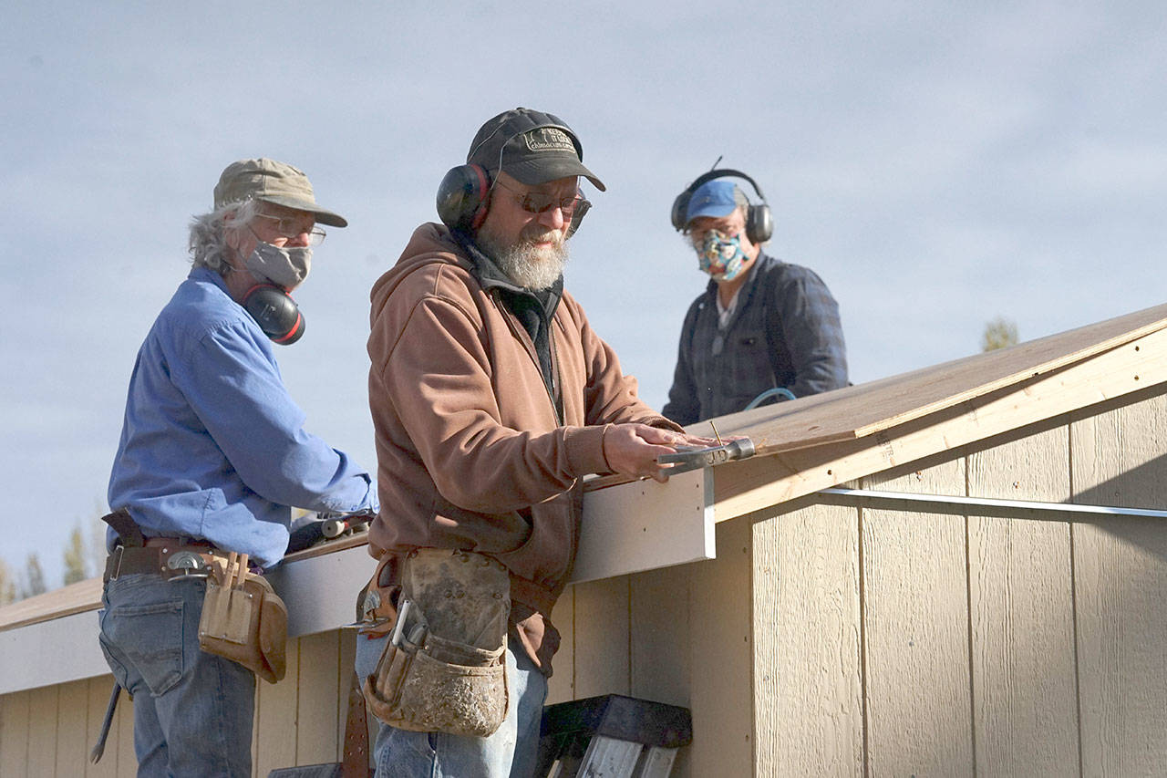 Larry Morrell, from left, Greg Kossow and Blue Heron Construction co-owner Randy Welle put a roof on an emergency shelter Thursday afternoon in Port Townsend. The neighbors formed a volunteer group to build one shelter over several days as part of the Community Build Project, which aims to provide temporary-use shelters for the homeless during the coming winter months. (Nicholas Johnson/Peninsula Daily News)