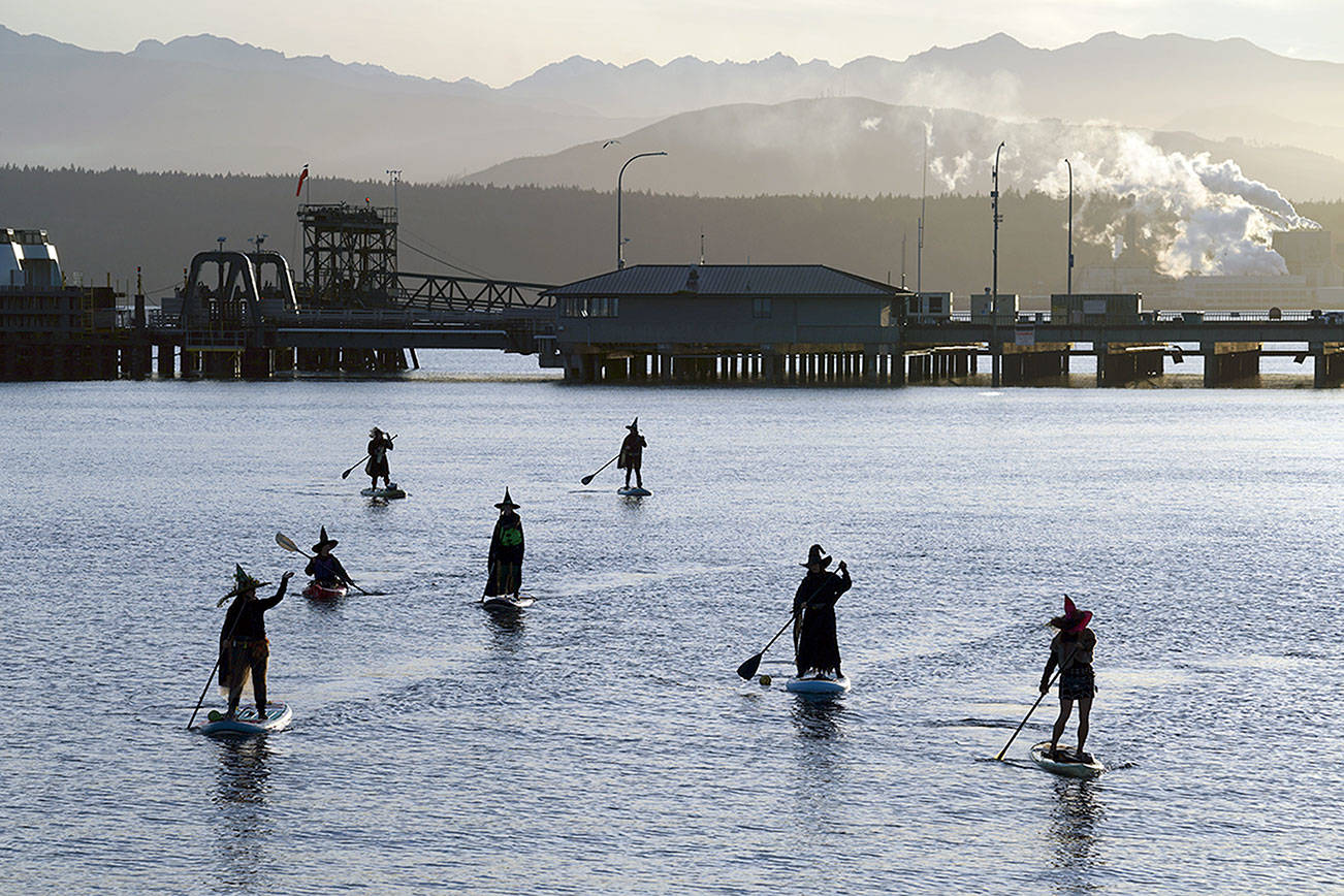 Cackling all the way, seven witches celebrate Halloween by paddling through Port Townsend Bay under a setting sun Saturday evening, with the ferry terminal, the paper mill and the Olympic Mountains in the background. This coven includes Juanita Maples, Shannon Murock, Heather Sessions, Karyn Stillwell, Adrian Olson, Amy Pacifera and Lily Murock. (Nicholas Johnson/Peninsula Daily News)