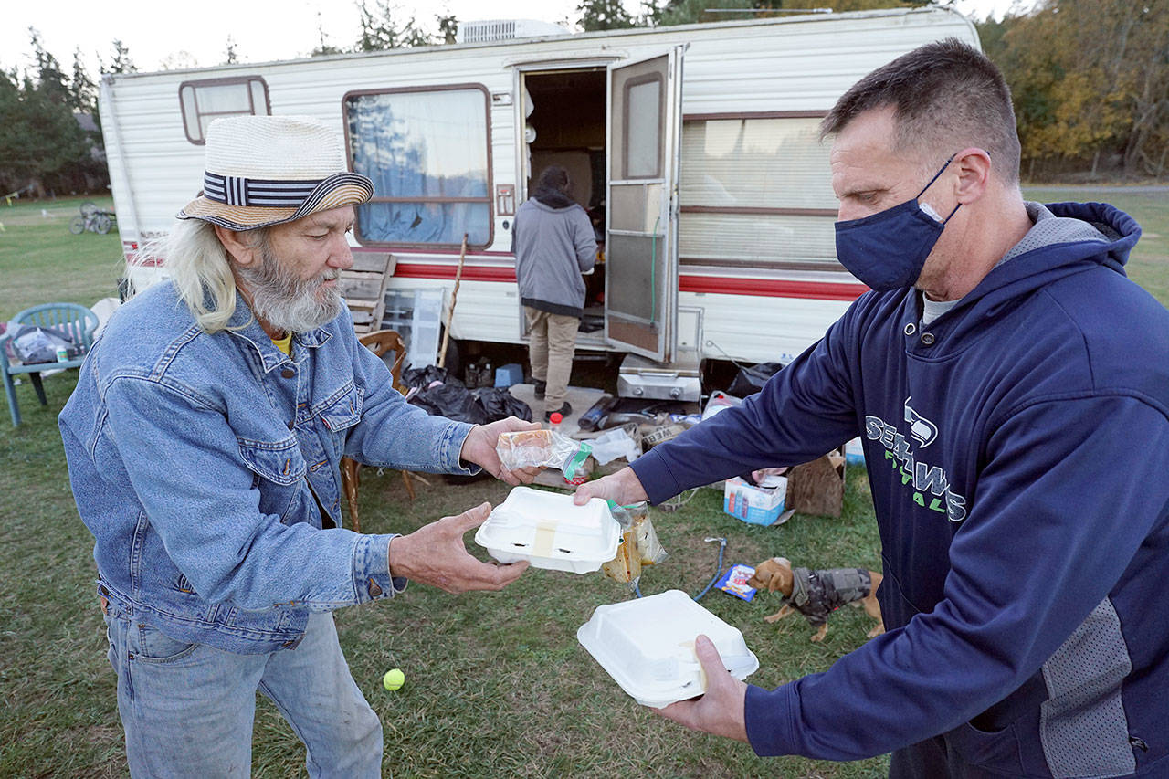 Chef Troy Murrell with Bayside Housing and Services, right, hands a hot meal to Richard Glaze on Sunday at the Jefferson County Fairgrounds campground. Glaze, a retired plumber who has been homeless in Port Townsend for about 9 years, has been living in a van at the fairgrounds since July. Glaze said he came to town from Spokane to be near family but couldn’t find a place to rent on his Social Security income. “Once you get stuck, you really get stuck,” he said. (Nicholas Johnson/Peninsula Daily News)
