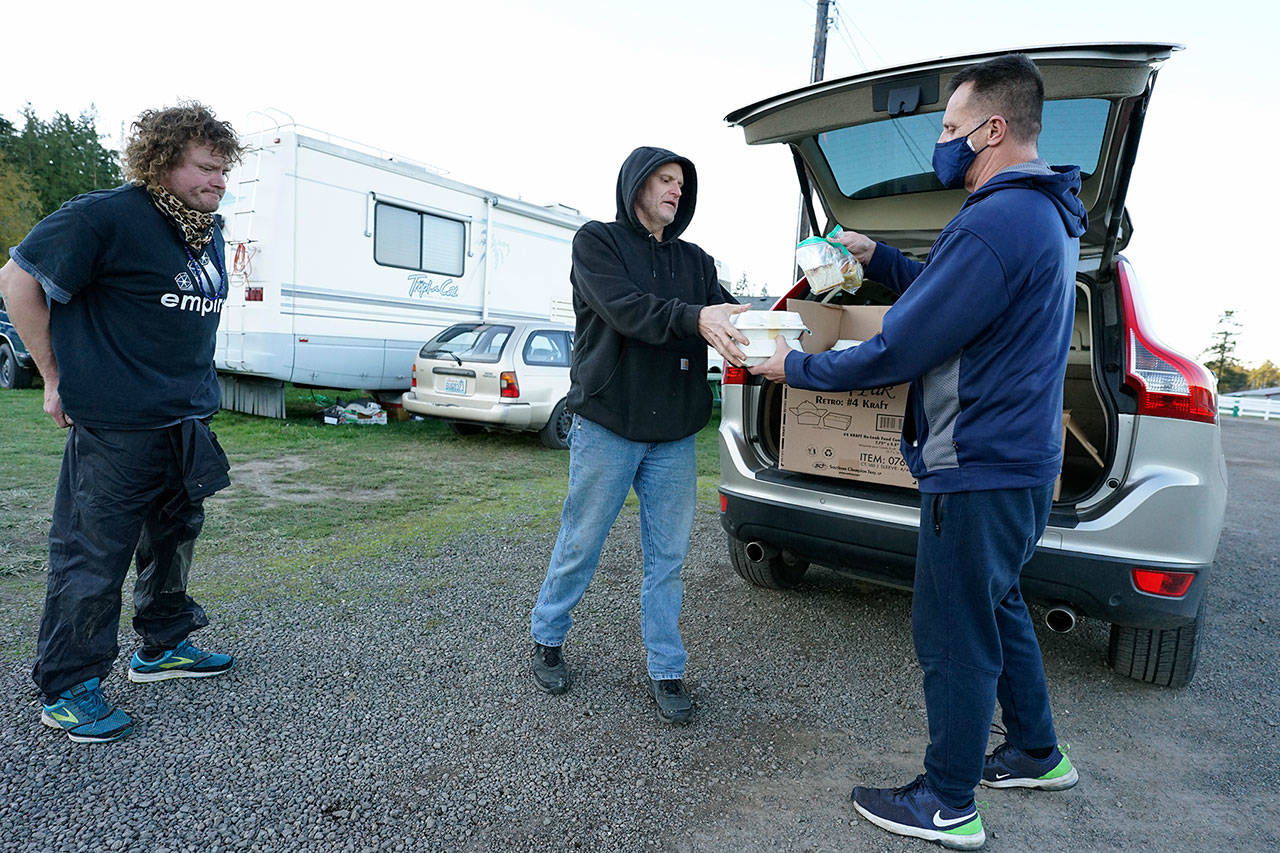 Chef Troy Murrell, right, hands a couple of hot meals to Brian Thompson, center, as Jason Guyett waits to get a meal of his own Sunday at the Jefferson County Fairgrounds campground in Port Townsend. Murrell, an employee of Bayside Housing and Services, is the chef at the Old Alcohol Plant Inn in Port Hadlock. (Nicholas Johnson/Peninsula Daily News)