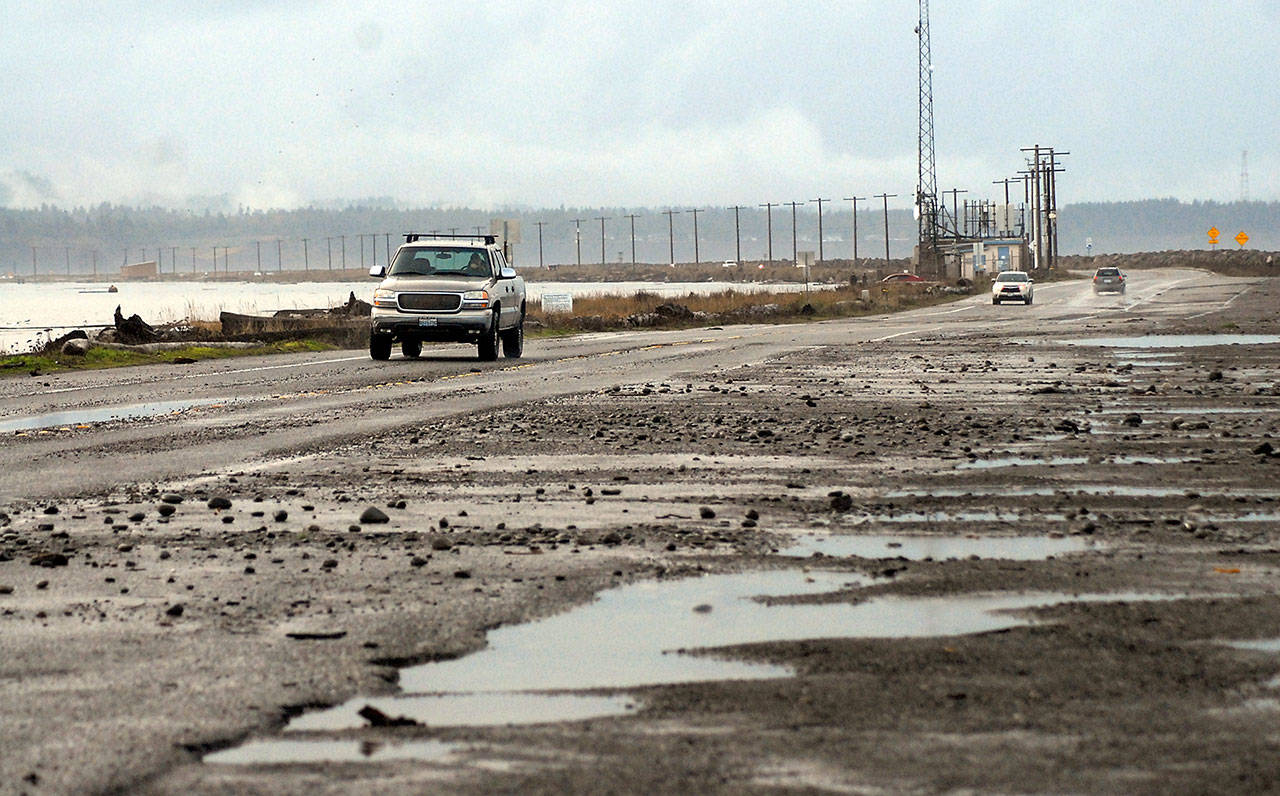Vehicles make their away along a rock-strewn stretch of Ediz Hook Road in Port Angeles after high waves pushed debris across a parking area and a section of roadway. (Keith Thorpe/Peninsula Daily News)