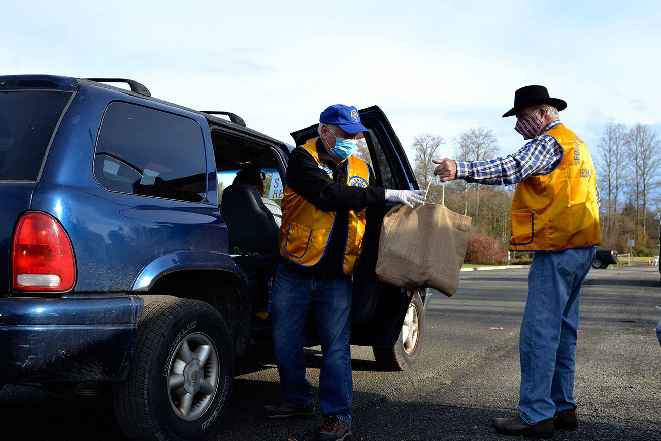 George Dooley, left, and Edward Alders with the Sequim Valley Lions Club work together to load a vehicle with food during the Family Holiday Meal Bag distribution program in Sequim.  Matthew Nash/Olympic Peninsula News Group