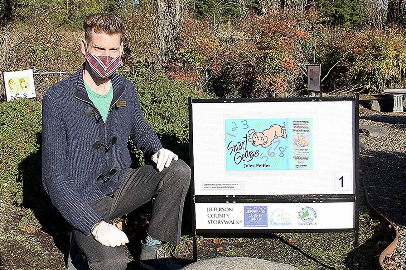 Scott Bahlmann, youth and teen services librarian at the Jefferson County Library, kneels next to the start of the storywalk outside the library. Bahlmann, along with public services manager Chris HoffmanHill, curated the three storywalks that are now located throughout Jefferson County. (Zach Jablonski/Peninsula Daily News)