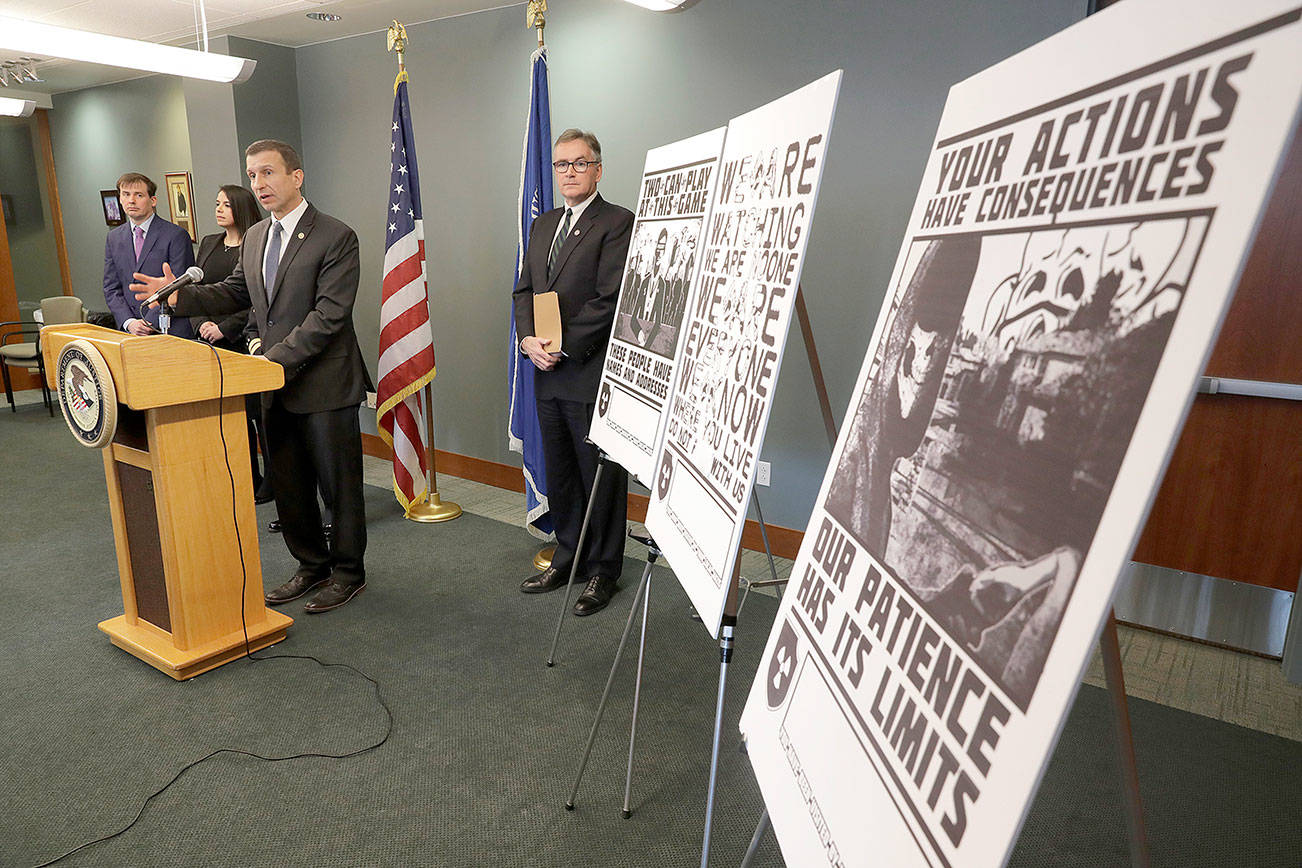 FILE - In this Feb. 26, 2020, file photo, Raymond Duda, FBI Special Agent in Charge in Seattle, speaks during a news conference at a podium, about charges against a group of alleged members of the neo-Nazi group Atomwaffen Division for cyber-stalking and mailing threatening communications, including the Swastika-laden posters at right, in a campaign against journalists in several cities. Johnny Roman Garza, an Arizona man has been sentenced to 16 months in prison for his role in a neo-Nazi group's coordinated campaign to threaten and harass journalists, activists and other targets on both U.S. coasts, Wednesday, Dec. 9, 2020.  (AP Photo/Ted S. Warren, File)
