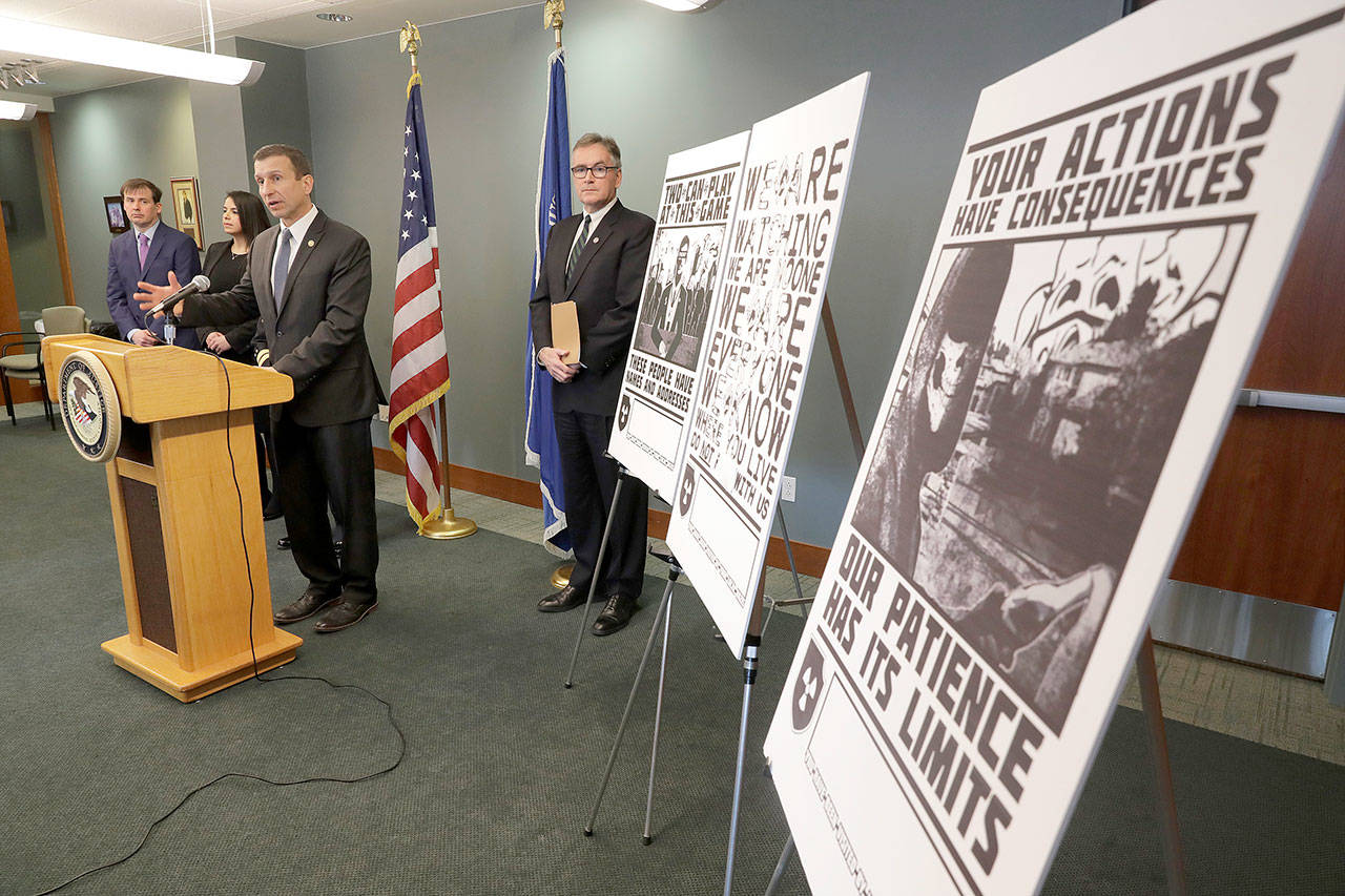 In this Feb. 26, 2020, file photo, Raymond Duda, FBI Special Agent in Charge in Seattle, speaks during a news conference at a podium, about charges against a group of alleged members of the neo-Nazi group Atomwaffen Division for cyber-stalking and mailing threatening communications, including the Swastika-laden posters at right, in a campaign against journalists in several cities. Johnny Roman Garza, an Arizona man has been sentenced to 16 months in prison for his role in a neo-Nazi groups coordinated campaign to threaten and harass journalists, activists and other targets on both U.S. coasts Wednesday, Dec. 9, 2020. (Ted S. Warren/Associated Press file)