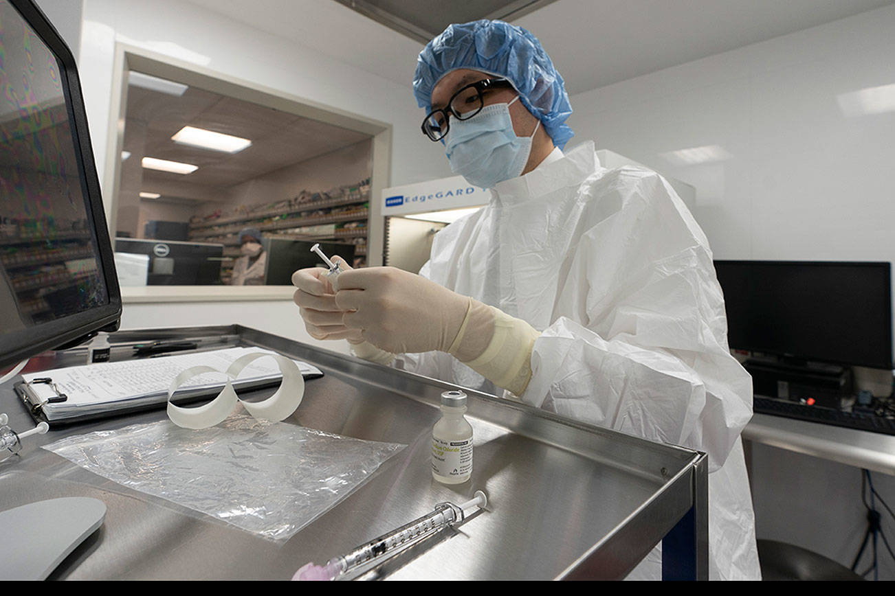 A pharmacist labels syringes in a clean room where doses of COVID-19 vaccines will be handled, Wednesday, Dec. 9, 2020, at Mount Sinai Queens hospital in New York. The hospital expects to receive doses once a vaccine gets the emergency green light by U.S. regulators. (AP Photo/Mark Lennihan)