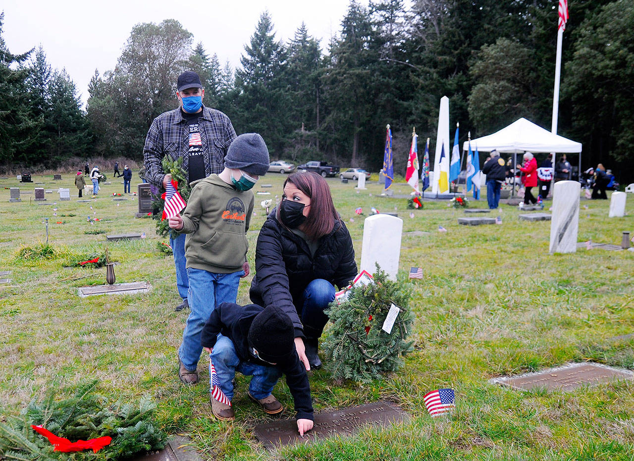 Jennifer Groves of Port Angeles helps sons Blake, 5 (standing), and 2-year-old Bryce, place a wreath on a veteran’s grave marker Saturday, as Groves’ stepfather Bobby Yaun looks on. Groves said she attended the event “to teach my men to show honor.” (Michael Dashiell/Olympic Peninsula News Group)