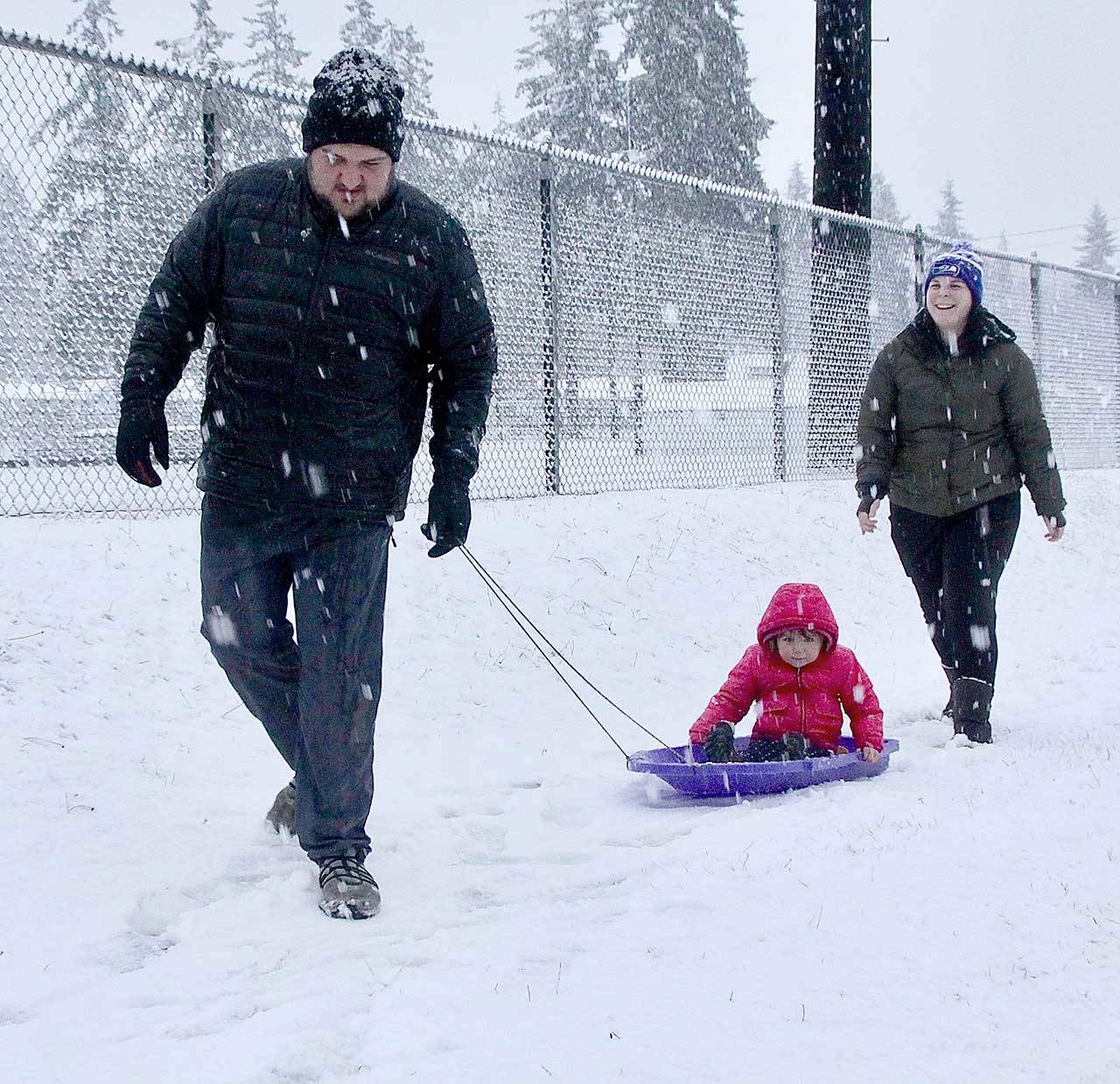 Jarrett and LeAnn Hansen took their daughter H.J., 2, out sliding just outside the fence of Elks Playfield on Pine Street on Monday during the first snow of the winter. (Dave Logan/for Peninsula Daily News)