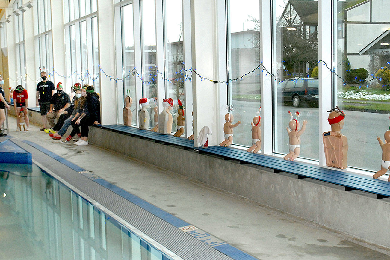 Keith Thorpe/Peninsula Daily News
Life guards and staff members at the Shore Aquatic Center in Port Angeles gather on Thursday near a display of first-aid training dolls decorated for Christmas and placed in the street-side windows of the center on West Fifth Street. Pool director Steve Burke said the display would probably remain in place at least through Christmas Day.