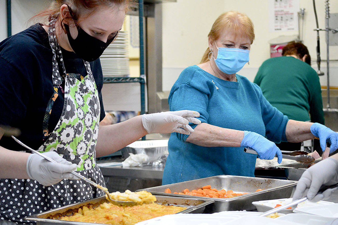 Volunteers Mya Lindstrom, left, and Judy Robinett direct the carrots and scalloped potatoes through the assembly line during the Tri-Area Community Center's Christmas dinner on Friday. Diane Urbani de la Paz/Peninsula Daily News