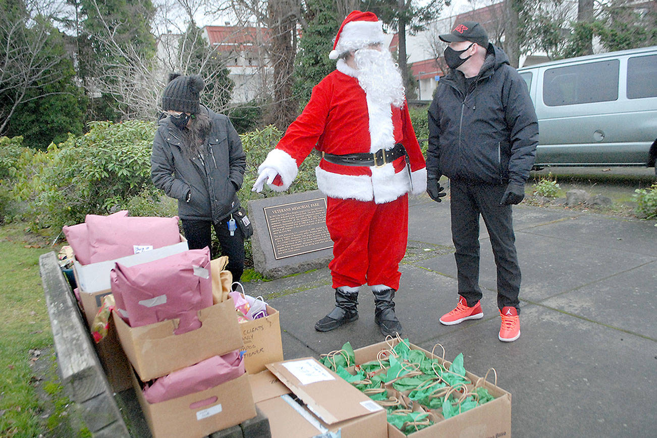 Keith Thorpe/Peninsula Daily News
Santa portrayed by shelter coordinator Casey Sawyer for Serenity House of Clallam County, gives gift-giving directions to Serenity House client Roger Smith, right, as Viola Ware of the Rediscovery Program looks on during meal and gift distribution at Veterans Park on Christmas Day in Port Angeles.