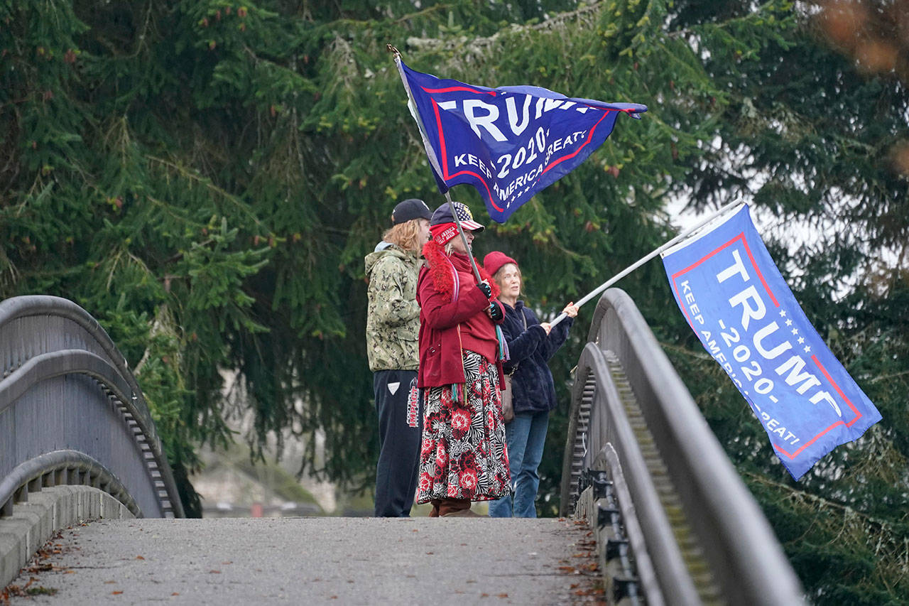 Three people stand and wave flags above morning traffic from a pedestrian overpass near the Capitol in Olympia on Thursday, the day after supporters of President Donald Trump protested in Olympia against the counting of electoral votes in Washington, D.C., to affirm President-elect Joe Biden’s victory. (Ted S. Warren/The Associated Press)