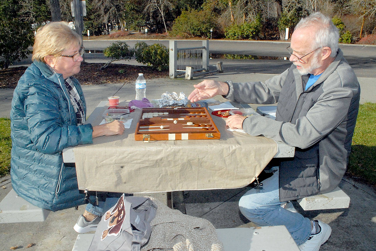 Susie and Larry Ormbrek of Sequim enjoy a sunny Tuesday, Jan. 19, to play a game of backgammon while eating lunch near the shore of Sequim Bay at John Wayne Marine in Sequim. The pair said they often try to take advantage of nice weather for outdoor dining. (Keith Thorpe/Peninsula Daily News)