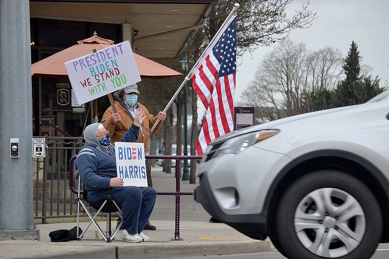 Steve Downer and Brian Grad, both of Sequim, wave to drivers on Wednesday as they celebrate the inauguration of President Joe Biden and Vice President Kamala Harris. Im relieved, Downer said of the inauguration. He hopes their first steps will be to address COVID-19, the economy and environment. (Matthew Nash/ Olympic Peninsula News Group)