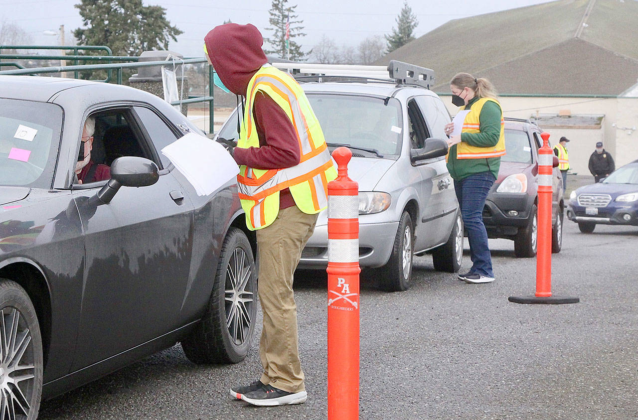 Volunteers Anthony Brigandi and Jennifer Rogers check out the next cars in line for their appointment to get a COVID-19 Pfizer vaccine Saturday morning at the Port Angeles High School campus. The whole process at the PAHS auxiliary gym and adjacent parking lot is run smoothly by over 60 volunteers from across the county and takes about 30 minutes. (Dave Logan/For Peninsula Daily News)