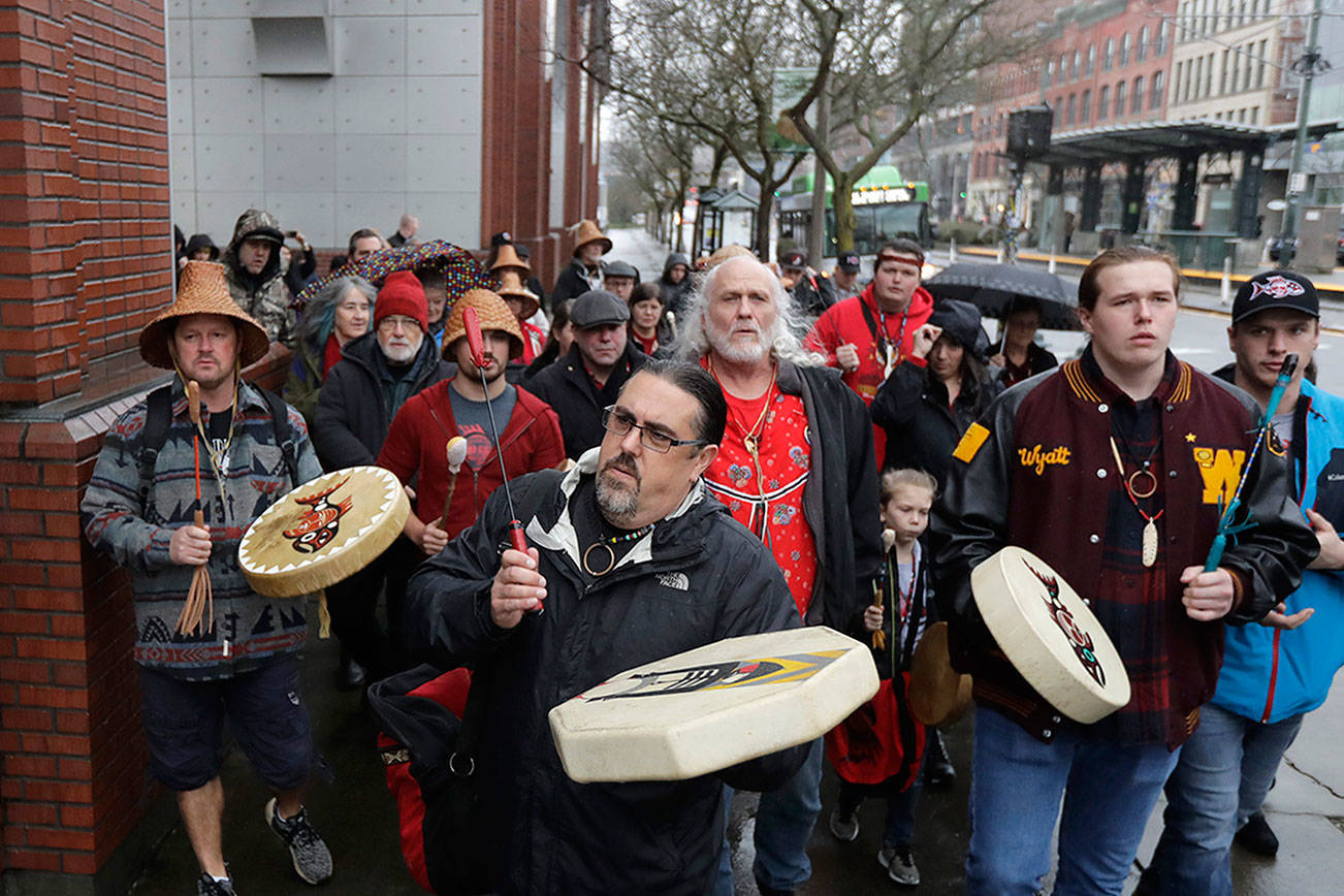 FILE - In this Jan. 6, 2020, file photo, Tony A. (Naschio) Johnson, center, elected chairman of the Chinook Indian Nation, plays a drum as he leads tribal members and supporters as they march to the federal courthouse in Tacoma, Wash., as they continue their efforts to regain federal recognition. As COVID-19 disproportionately affects Native American communities, many tribal leaders say the pandemic poses particular risks to tribes without federal recognition. The Chinook Nation received some federal funding through a local nonprofit for small tribes to distribute food to elders and help with electricity bills, tribal Johnson said. (AP Photo/Ted S. Warren, File)