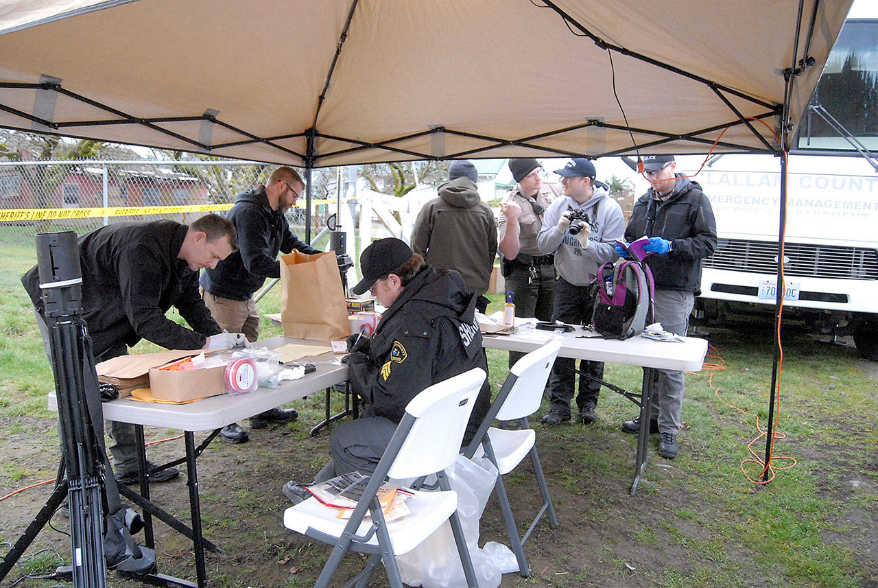 <address>Investigators from the Clallam County Sheriff’s Office and other agencies examine evidence collected on Friday from a residence on Lower Elwha Road west of Port Angeles where a suspect in December’s triple homicide was arrested on Thursday. (Keith Thorpe/Peninsula Daily News)</address>