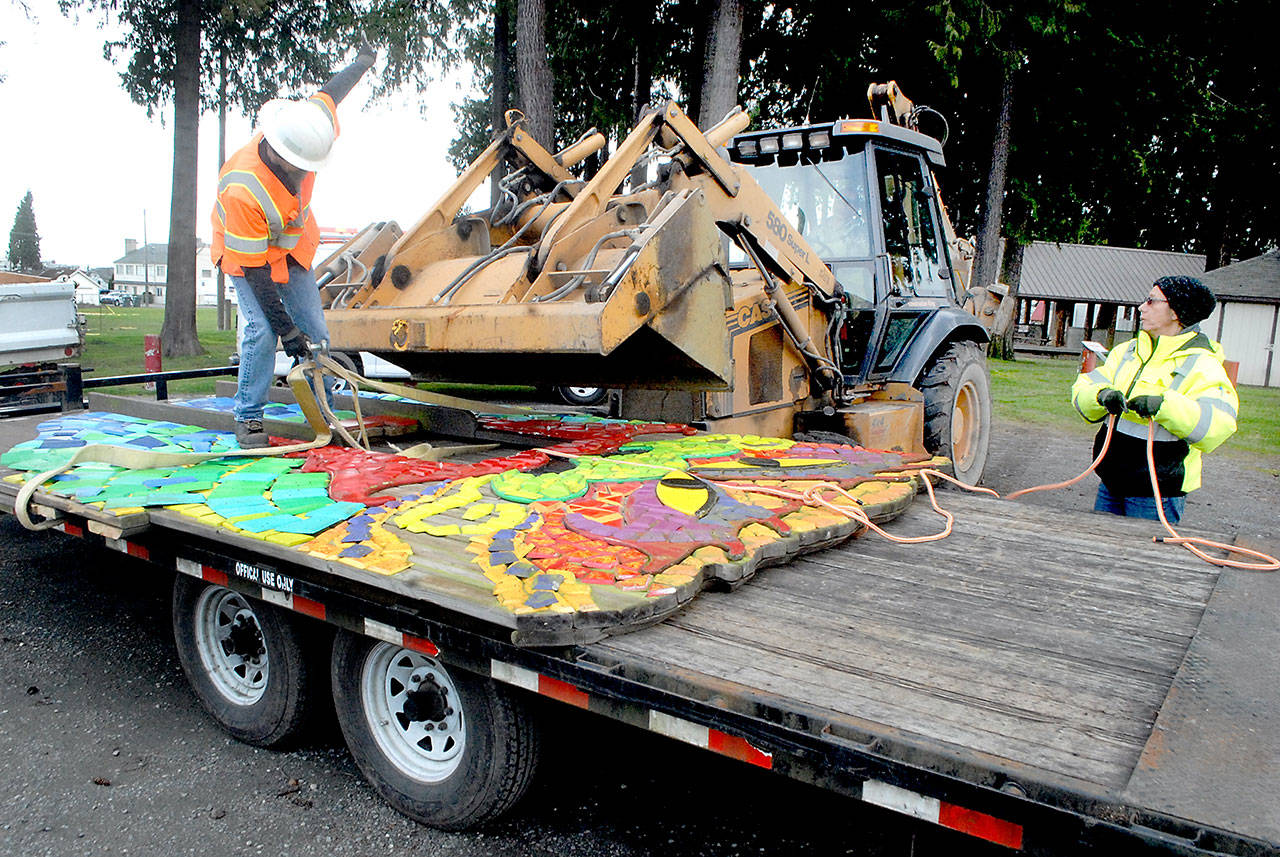 Port Angeles Parks and Recreation worker Darryl Anderson, left, signals to bulldozer operator Leon Leonard as fellow employee Brooke Keohokalole curls up a guide rope after the dragon mosaic from the Dream Playground at Erickson Playfield is lowered onto a trailer earlier this week in Port Angeles. Demolition has begun on the mostly wooden playground, originally built by volunteer labor in September 2002, to make way for modernized playground equipment later this year. The dragon, which once had a playground slide coming from its nose, will be put into storage and later incorporated into the new playground. (Keith Thorpe /Peninsula Daily News)