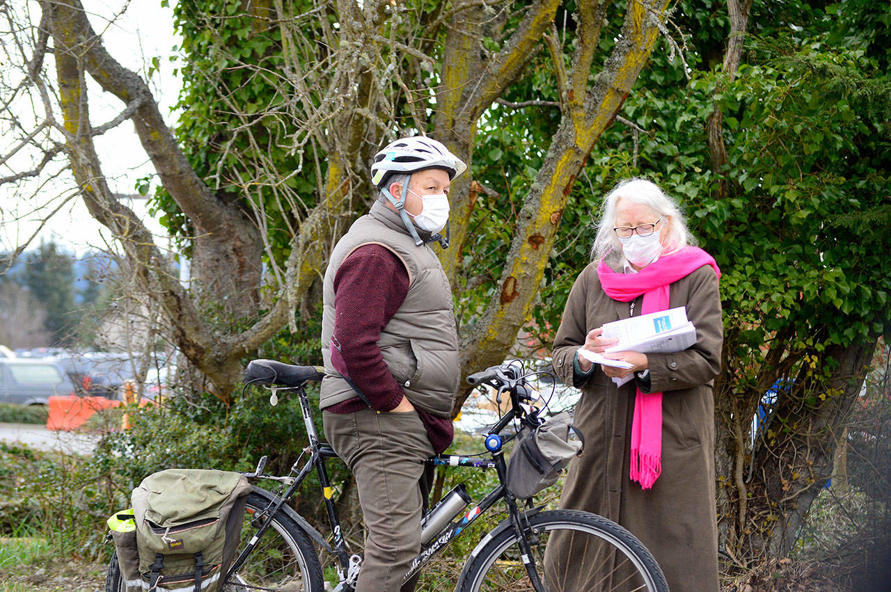 Gerry Kress of Port Townsend pedaled his bike to Jefferson Healthcare’s drive-through COVID-19 vaccination site Tuesday morning, where vaccinator Viviann Kuehl of Quilcene briefed him on the procedure. Kress was among 375 people scheduled for first doses of the Pfizer vaccine. (Diane Urbani de la Paz/Peninsula Daily News)
