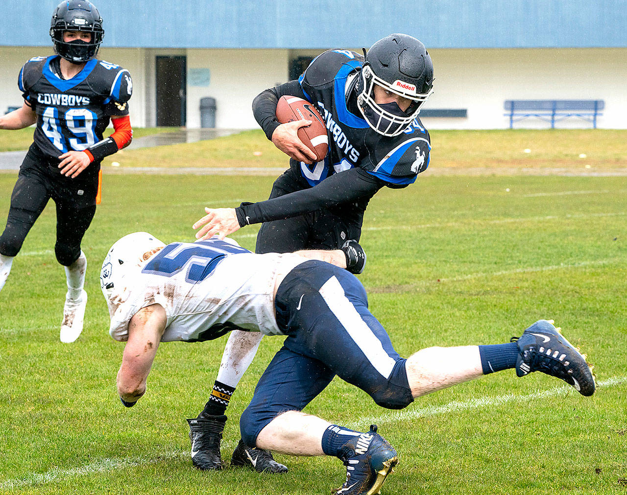 East Jefferson’s Lonnie Kenney (49) watches as teammate Logan Massie (34) pivots around Cascade Christian’s Ryan Hersey to pick up yardage in a game played in Chimacum on Saturday. (Steve Mullensky/for Peninsula Daily News)