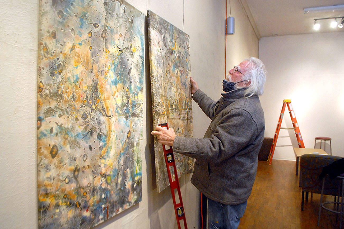 Bob Stokes, owner of Studio Bob in Port Angeles, hangs artworks on the wall of his art and music venue on Wednesday in preparation for Friday’s “Save the Bob” live-streaming music fundraiser. (Keith Thorpe/Peninsula Daily News)