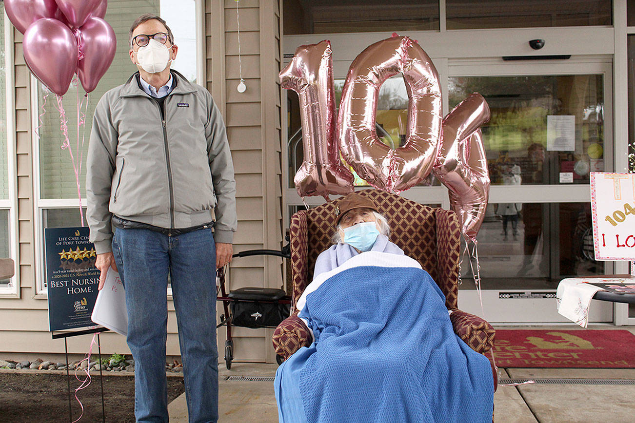 Jim Hansen, left, stands with his mother Lorraine on Friday during a drive by celebration of her 104th birthday on Saturday at the Port Townsend Life Care Center. The local law enforcement, first responders, and friends and family of Lorraine drove through waving and wishing her well. (Zach Jablonski/Peninsula Daily News)