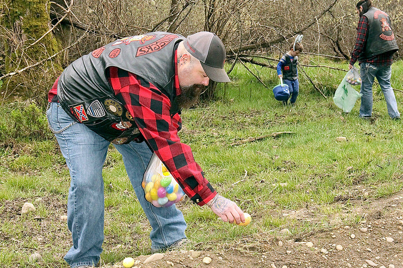 Dave Logan/for Peninsula Daily News
Jason Chapman, a member of the Cllalm Colunty chapter of the Roughnecks Motorcycle Club, places an egg in a clearing near West 10th Street and Estes Court in west Port Angeles on Saturday so that neghborhood children could hunt Easter eggs today. Egg My Yard is a fundraising project for the nonprofit group made up of law enforcement and first responders. It will support support their annual “Shop with a Roughneck” in December. Club members take Clallam County foster children Christmas shopping, giving each child $100 to spend.