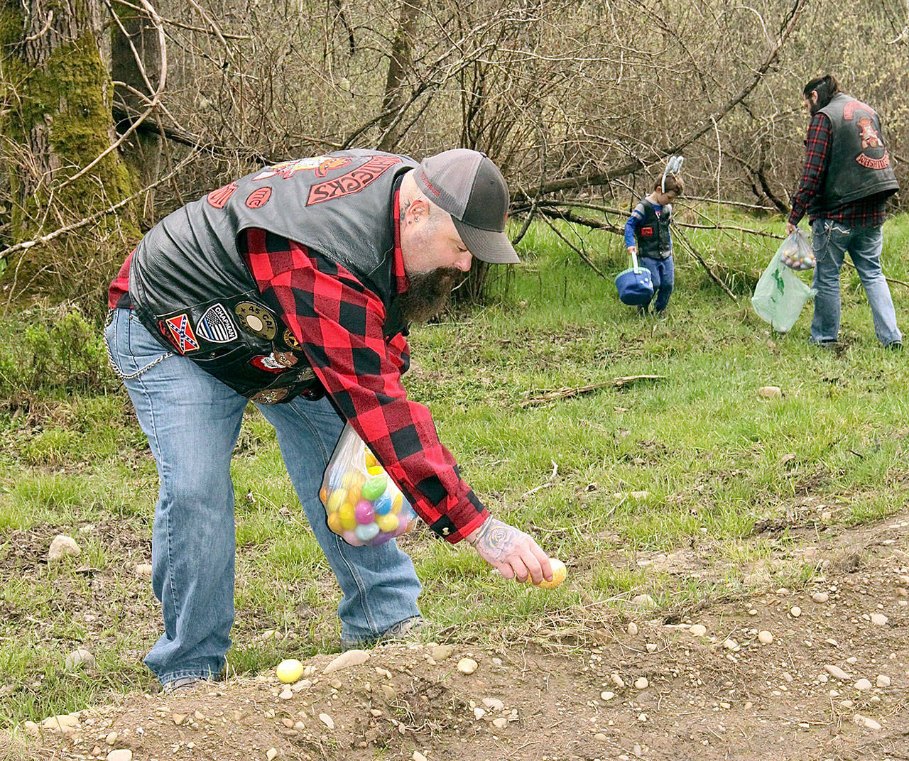 Jason Chapman, a member of the Clallam County chapter of the Roughnecks Motorcycle Club, places an egg in a clearing near West 10th Street and Estes Court in west Port Angeles on Saturday so that neighborhood children could hunt Easter eggs today. Egg My Yard is a fundraising project for the nonprofit group made up of law enforcement and first responders. It will support their annual “Shop with a Roughneck” in December. Club members take Clallam County foster children Christmas shopping, giving each child $100 to spend. (Dave Logan/for Peninsula Daily News)