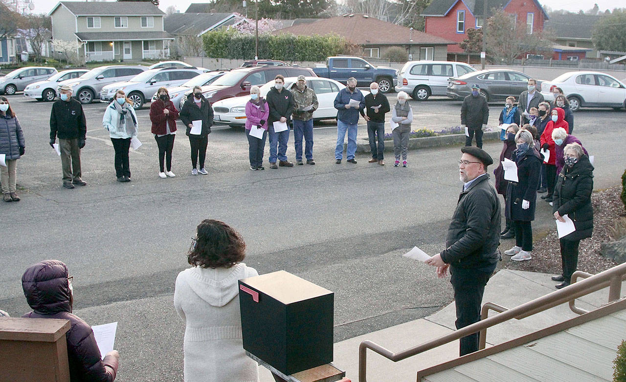 The First Presbyterian Church of Port Angeles held an Easter Sunrise Service modified to meet COVID-19 protocols. Almost 50 worshippers gathered in a circle near the back entrance of the church at 7 a.m. in sunny weather but 40 degrees. The group sang songs and heard the story of Jesus’ resurrection. The Rev. Matt Paul, in beret, leads the service while Bruce Emery played the music. (Dave Logan/for Peninsula Daily News)