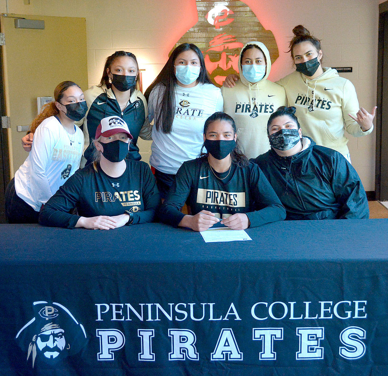 Gina Brown, center, sitting, signs to play with the Peninsula College women’s basketball court. At left is Peninsula women’s coach Alison Crumb. (Peninsula College)
