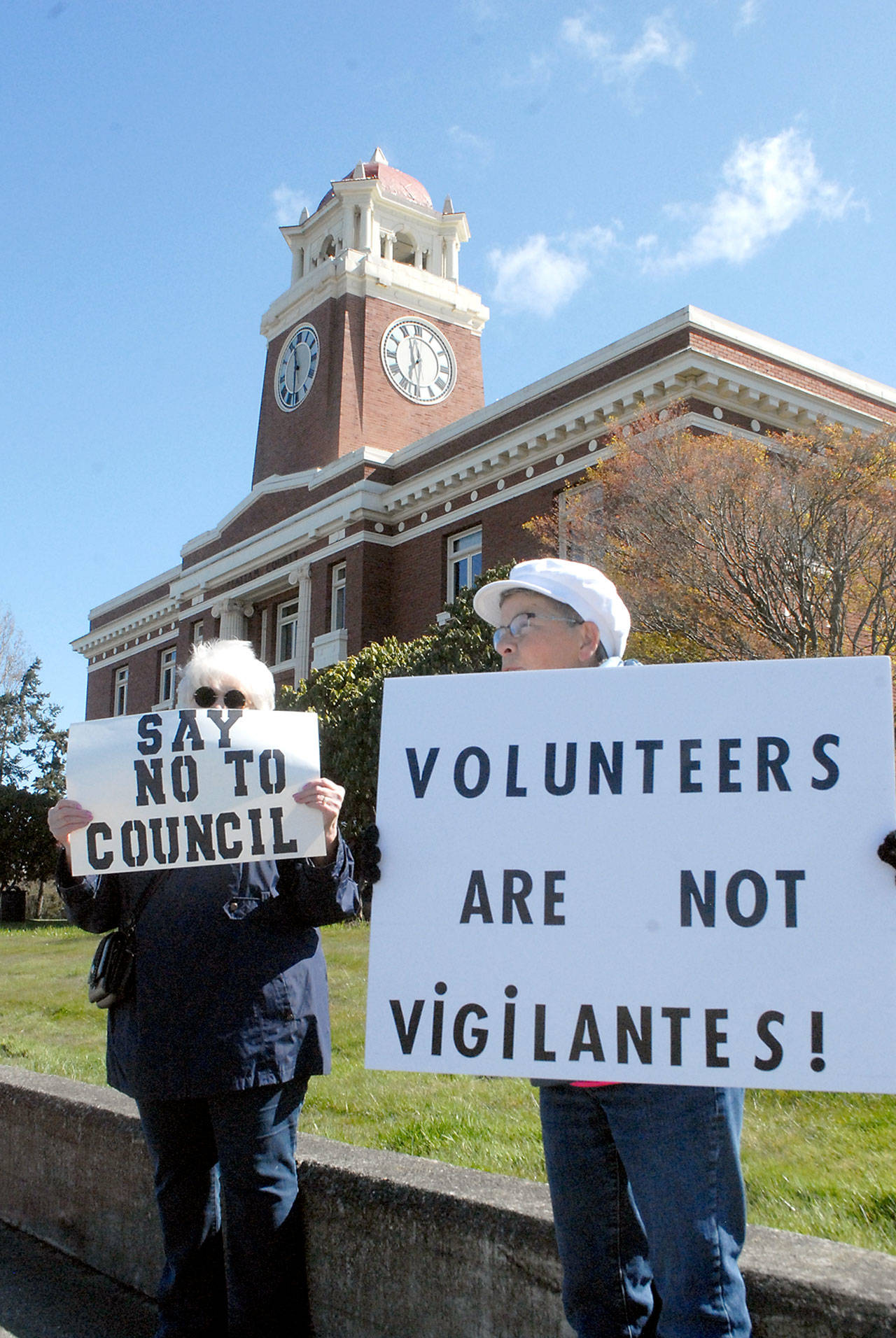 Darlene Heskett, left, and Patty Pastore hold signs on Saturday in front of the Clallam County Courthouse in Port Angeles protesting what they said is inaction by the Port Angeles City Council in handling homelessness and drug abuse in the city, as well as having been termed “vigilantes” for their cleanup efforts. The pair were part of a group of about 15 people taking part in the protest. (Keith Thorpe/Peninsula Daily News)