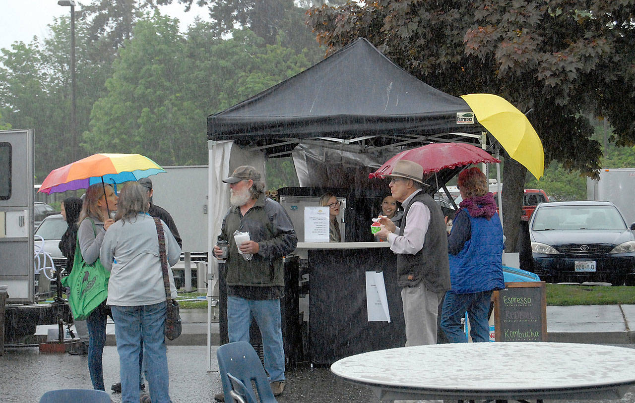 News Festival patrons stand in a pouring rain at a food booth during the 2019 Juan de Fuca Festival of the arts. (Keith Thorpe/Peninsula Daily)