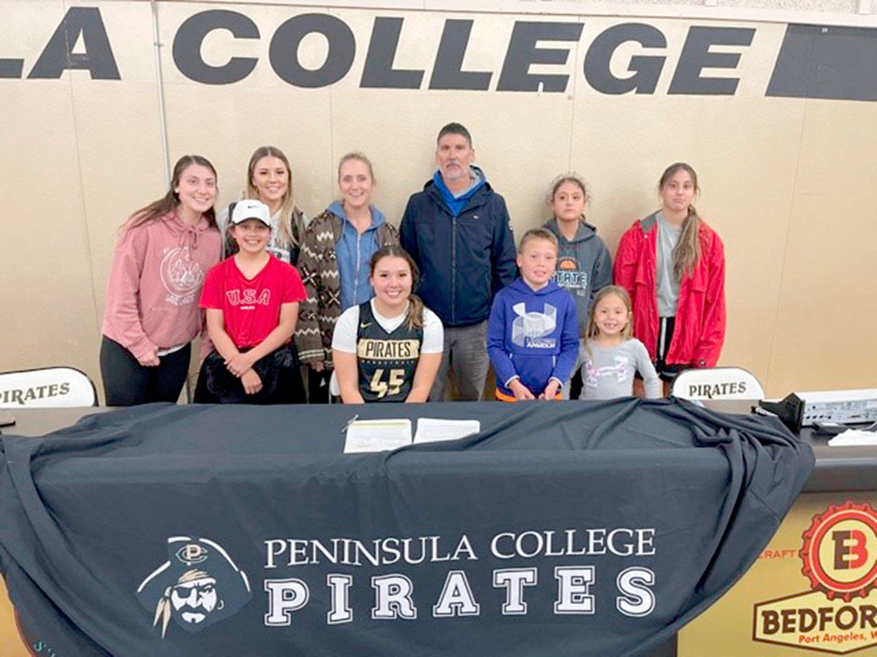 Neah Bay’s Ruth Moss, seated wearing No. 45, is joined by her family, including parents Robert and Cinnamon Moss, as she signs a letter of intent to play basketball at Peninsula College.