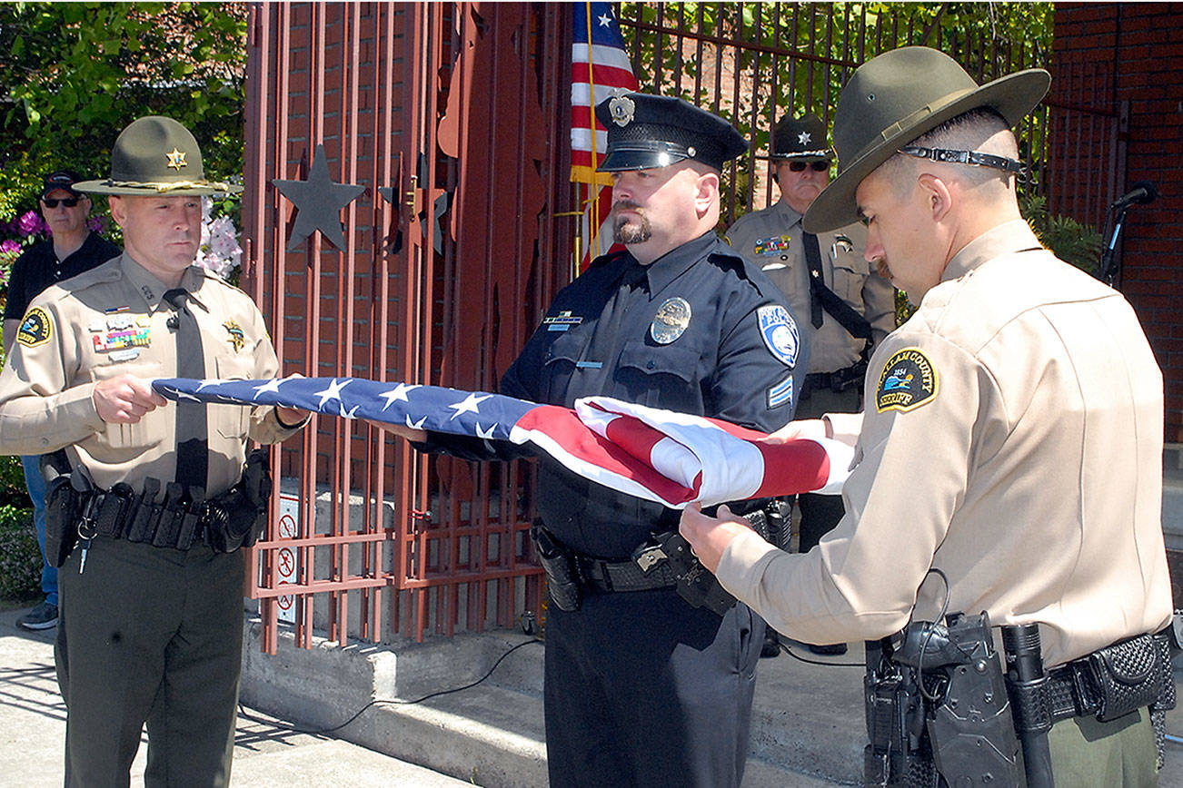 Keith Thorpe/Peninsula Daily News
Color guard members Deputy Eric Morris, left, and Deputy Hector Eagan, both of the Clallam County Sheriffs Officed, get assistance from Port Angeles police Detective Cpl. Dave Arand dring a flag folding ceremony at Friday's Peace Officers Memorial Day observance at Veteran's Park in Port Angeles. The event was part of Police Week, running May 9 throgh May 15, which honors law enforcement  officers and those killed in the line of duty.