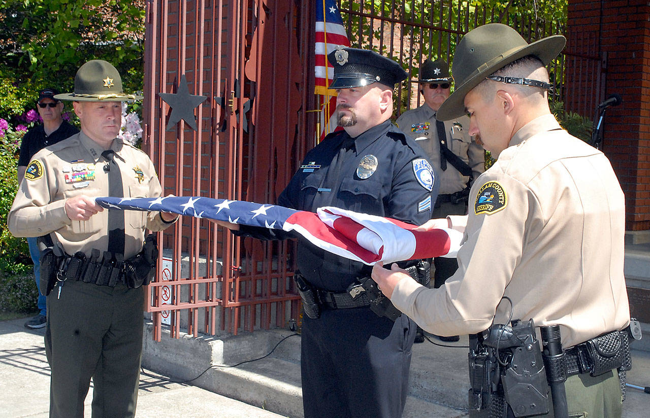 Color guard members Deputy Eric Morris, left, and Deputy Hector Eagan, both of the Clallam County Sheriffs Office, get assistance from Port Angeles police Detective Cpl. Dave Arand during a flag folding ceremony at Friday’s Peace Officers Memorial Day observance at Veteran’s Park in Port Angeles. The event was part of Police Week, running May 9 through May 15, which honors law enforcement officers and those killed in the line of duty. (Keith Thorpe/Peninsula Daily News)