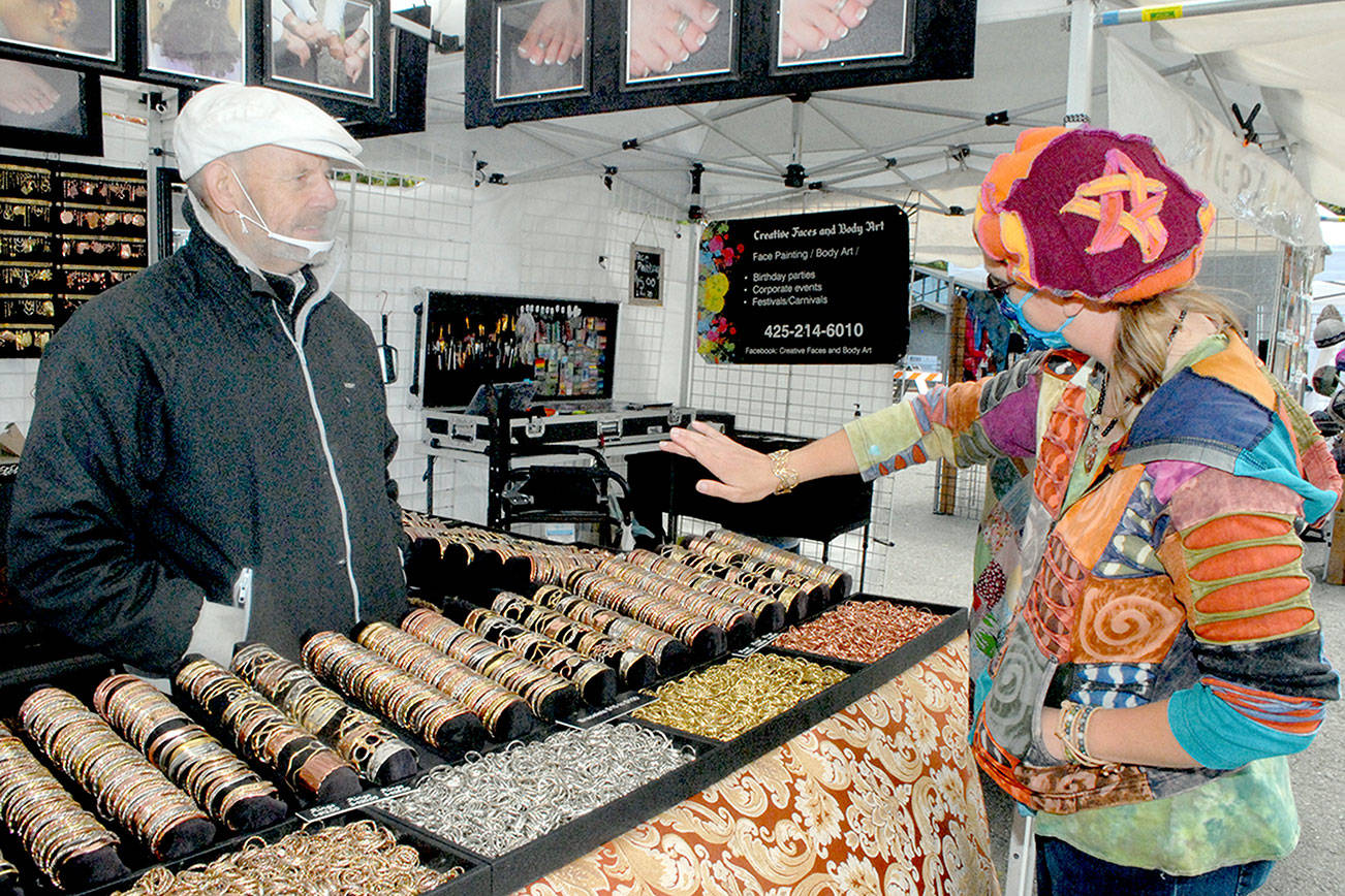 Keith Thorpe/Peninsula Daily News 

Saffrel Cochon of Monroe, right, tries on a bracelet as vendor Larry Rankin of Leavenworth-based Art to Suit You looks on at the Juan de Fuca Festival street fair outside the Vern Burton Community Center in Port Angeles. Admission to the fair, which runs through 6 p.m. today, is free. In-person concerts inside the community center continue today with limited tickets. More than 20 performances from multi-genre bands, singer-songwriters, dance ensembles and solo artists across North America are available for streaming on demand until June 30. More details are at JFFA.org/festival.