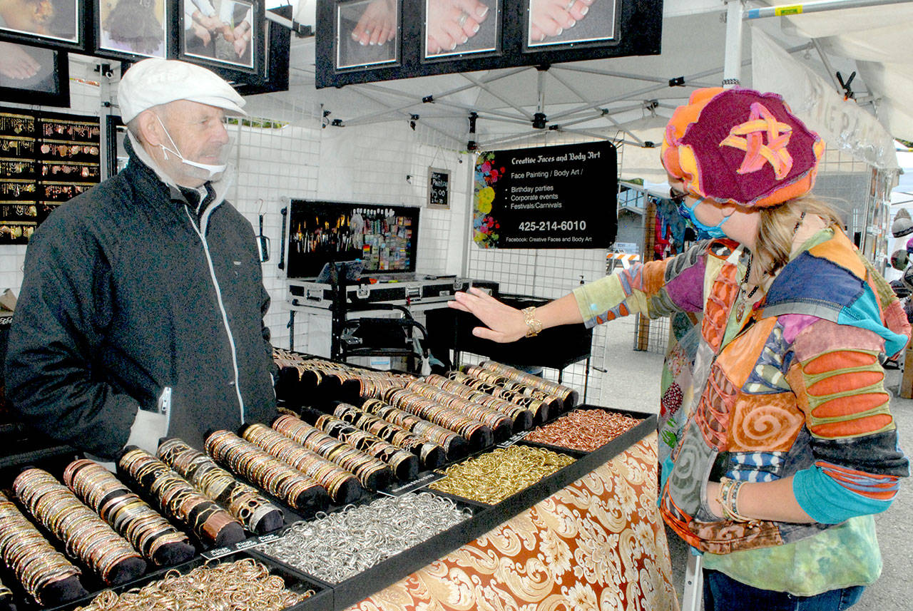 Saffrel Cochon of Monroe, right, tries on a bracelet as vendor Larry Rankin of Leavenworth-based Art to Suit You looks on at the Juan de Fuca Festival street fair outside the Vern Burton Community Center in Port Angeles. (Keith Thorpe/Peninsula Daily News)