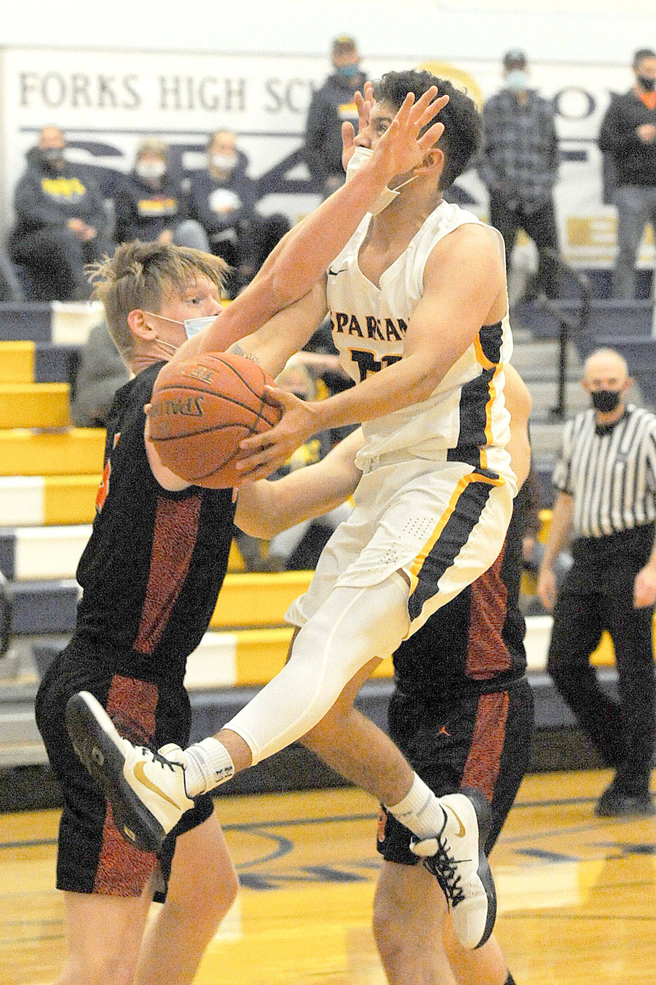 (Lonnie Archibald/for Peninsula Daily News) Forks Tony Hernandez-Flores drives towards the basket past Rainier’s Logan Bowers during this district play-off Monday game in Forks. The Spartans lost 61-56 to the Mountaineers.