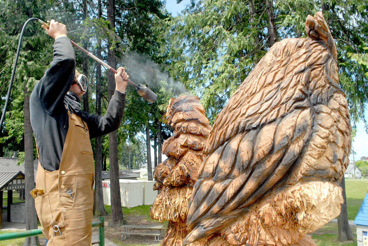 Carver Jeff Eshom uses a gas torch on Thursday to burn sections of a wood sculpture his is creating at the site of the new Dream Playground at Erickson Playfield in Port Angeles. (Keith Thorpe/Peninsula Daily News)