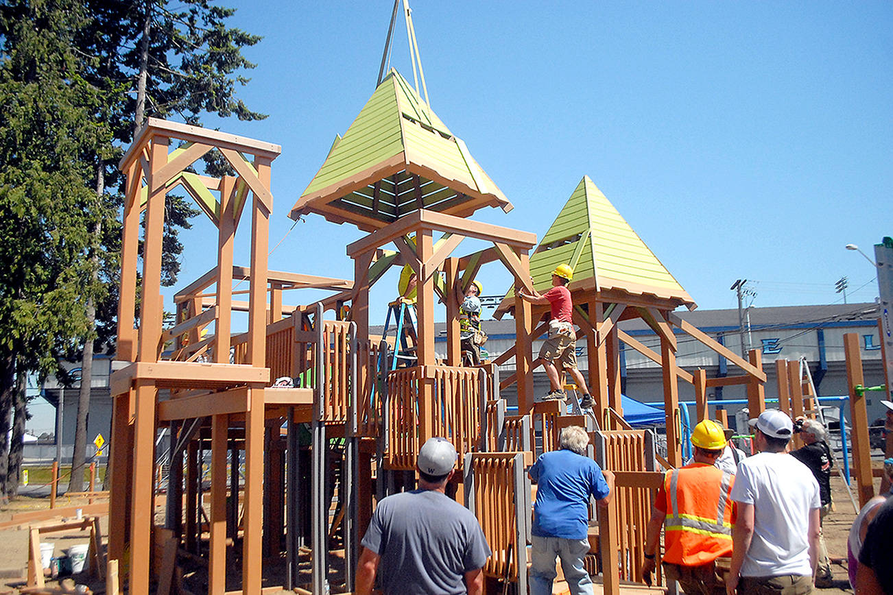 Volunteers work to secure a turret as it is lowered by crane on Sunday, the final day of the community build for the Generation II Dream Playground at Erickson Playfield in Port Angeles. (Keith Thorpe/Peninsula Daily News)
