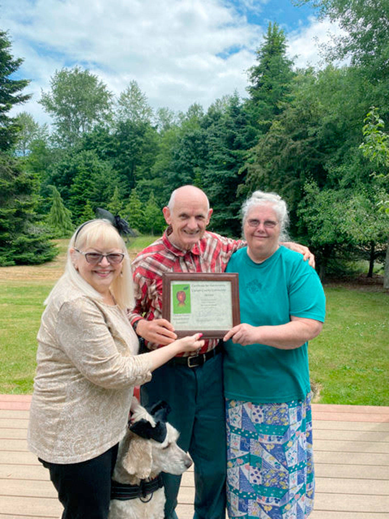 Lora Brabant, left, presents the Clallam County School Retirees Association’s 2021 Community Service Award to Ray and Ginni Weigel, also pictured is Daisy, the service dog. The Weigels were recognized for their support of the community through children’s book drives, cleaning trails, tutoring within the Port Angeles School District and other volunteer services.