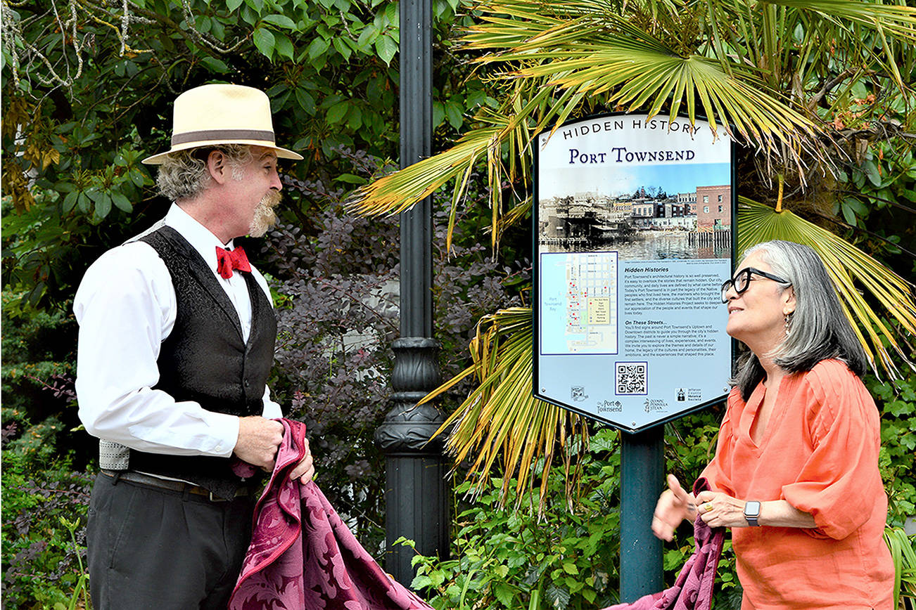 Historian Nathan Barnett of Olympic Peninsula Steam and Port Townsend Mayor Michelle Sandoval unveil a guide to the new “Hidden History” signs Thursday afternoon at Washington and Taylor streets. Fourteen interpretive signs, each revealing a facet of the city’s past, are being posted around Uptown and downtown Port Townsend. (Diane Urbani de la Paz/Peninsula Daily News)