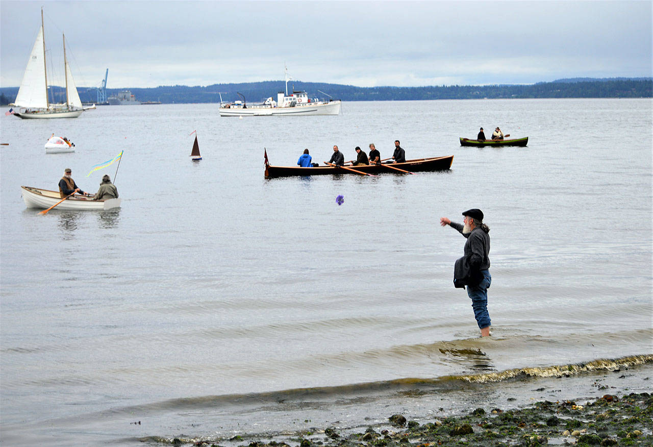Len Feldman sends flowers to Port Townsend Bay in honor of Brion Toss, the famed rigger, teacher and author who died in June 2020. The smallest boat on the water, a one-fifth scale model of a 1933 Sam Crocker-designed catboat named Katy, was launched during the procession Wednesday morning; it bears Toss’ ashes. (Diane Urbani de la Paz/Peninsula Daily News)