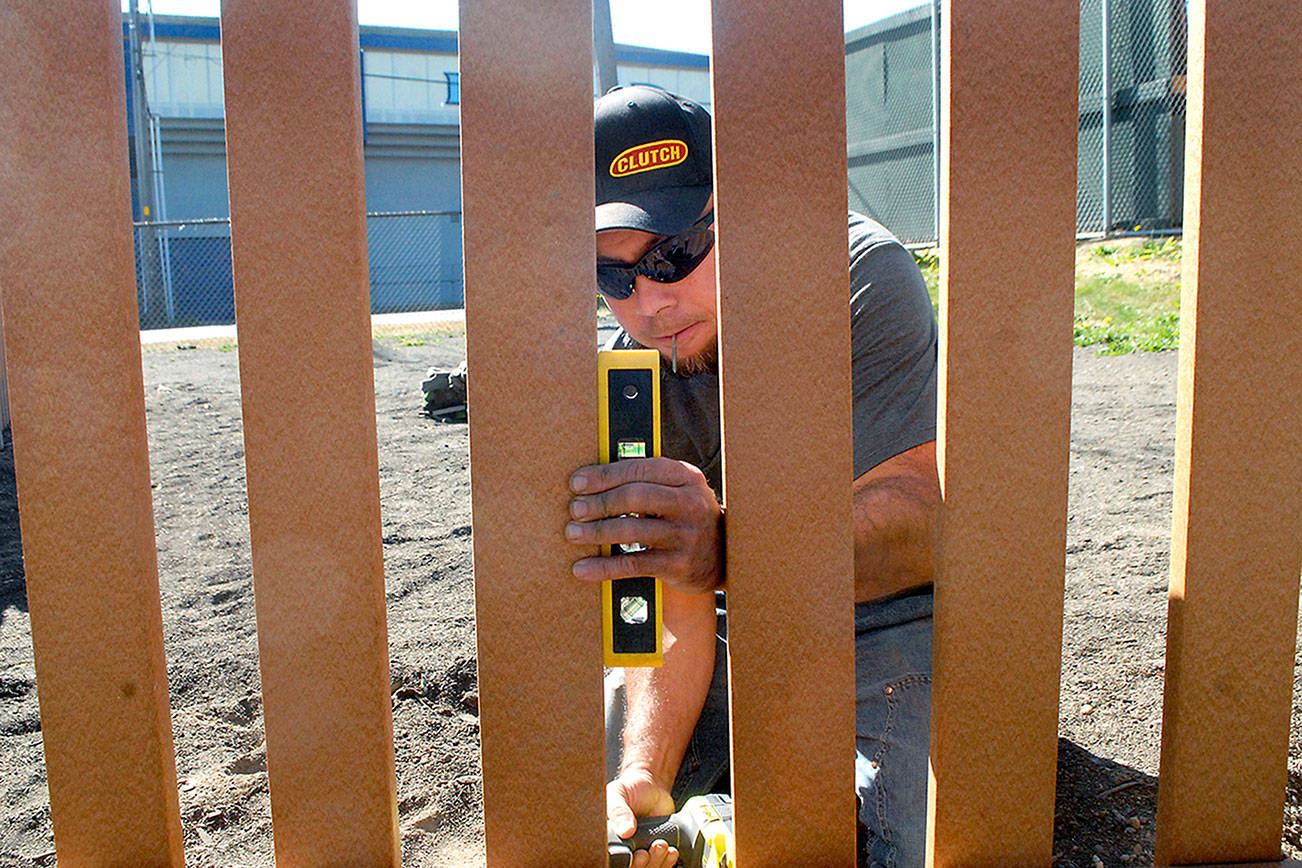 Charles Alice of Port Angeles uses a level to line up pickets in a fence around the Generation II Dream Playground at Erickson Playfield in Port Angeles on Sunday. (Keith Thorpe/Peninsula Daily News)