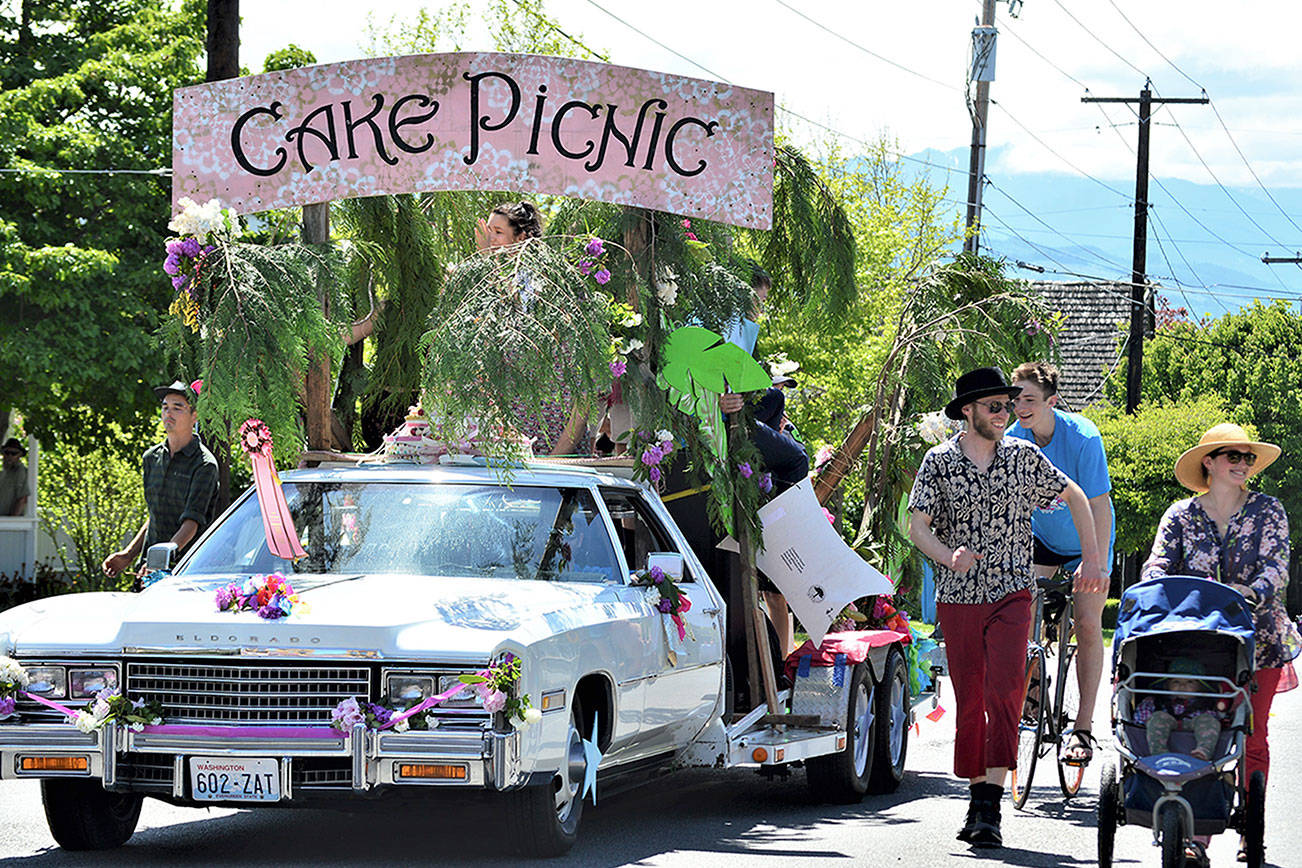Among the entrants coming back to the Rhody Festival Grand Parade is the Cake Picnic Cadillac, pictured in the 2019 parade through Uptown Port Townsend. Flanking the float are bicyclist Tao Johnston, pedestrian Ryan Charrier and Meredith Milholland with daughter Gitte, then 1, in her stroller. (Diane Urbani de la Paz/Peninsula Daily News)