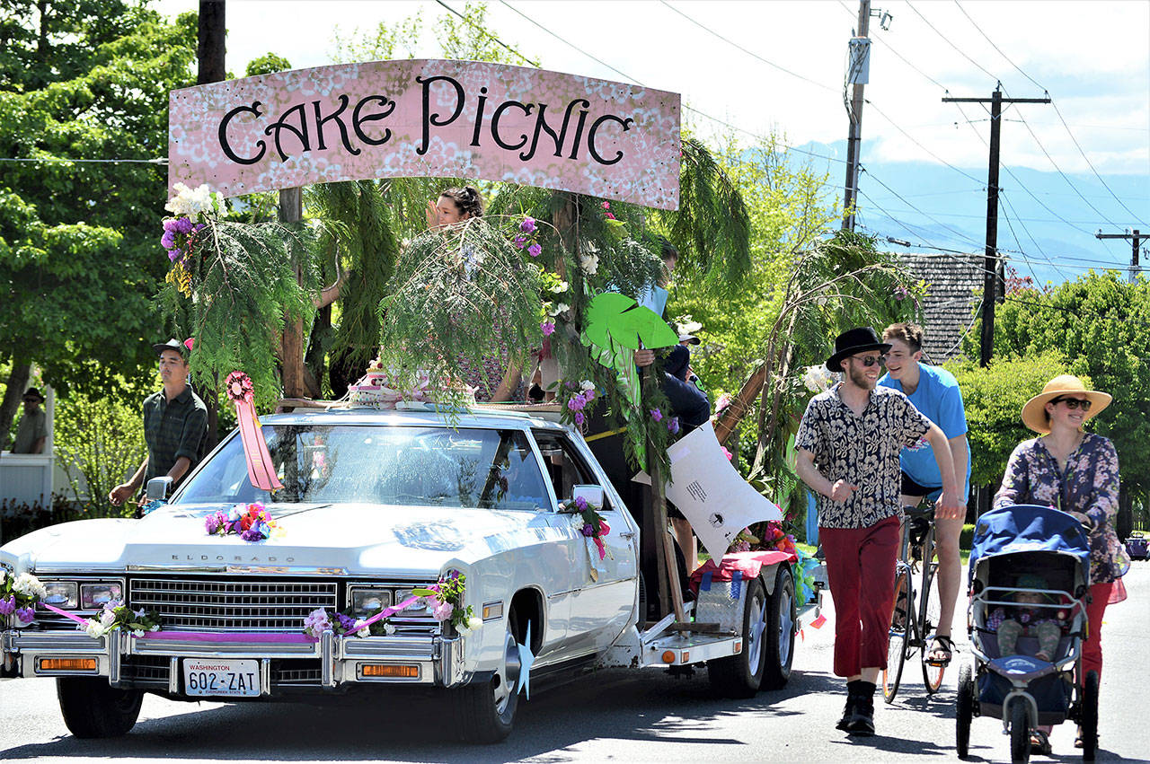 Among the entrants coming back to the Rhody Festival Grand Parade is the Cake Picnic Cadillac, pictured in the 2019 parade through Uptown Port Townsend. Flanking the float are bicyclist Tao Johnston, pedestrian Ryan Charrier and Meredith Milholland with daughter Gitte, then 1, in her stroller. (Diane Urbani de la Paz/Peninsula Daily News)